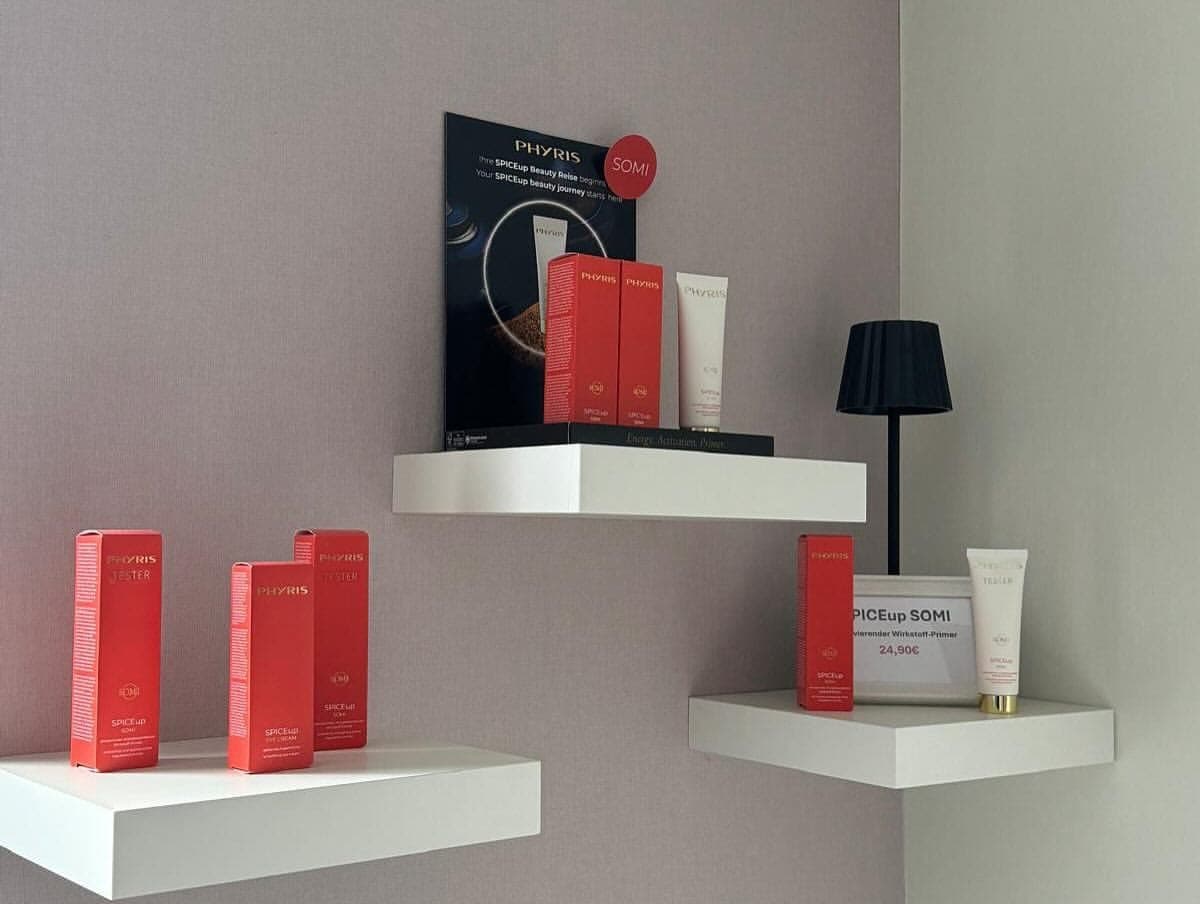 Wandboards im Institut mit einer PHYRIS-Pflegeserie und einer kleinen Tischleuchte vor der ruhigen rosé-grauen Wand.