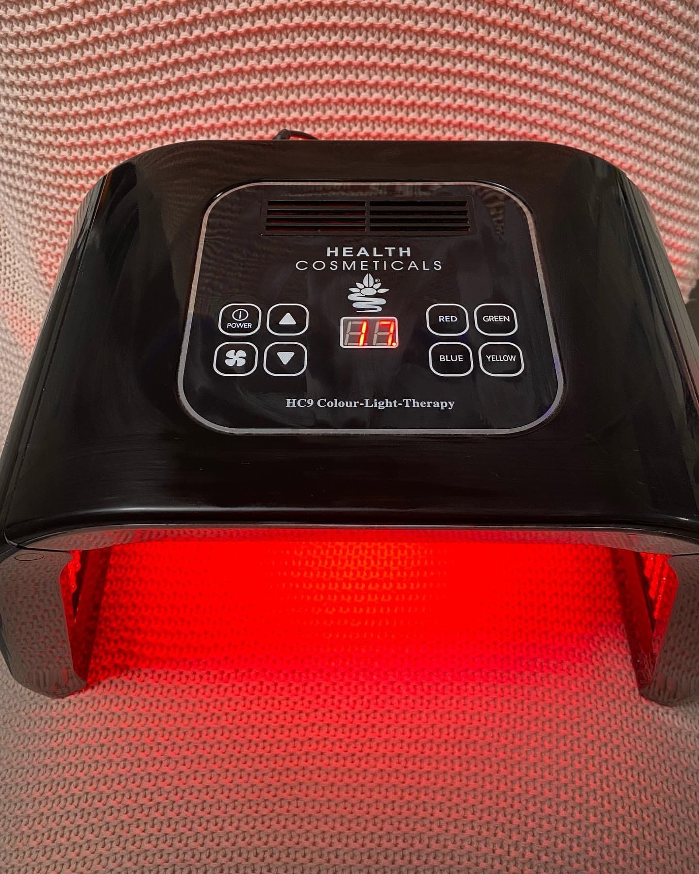 Das HC9 Lichttherapie-Gerät über der Behandlungsliege, die LED-Flächen leuchten warm rot.
