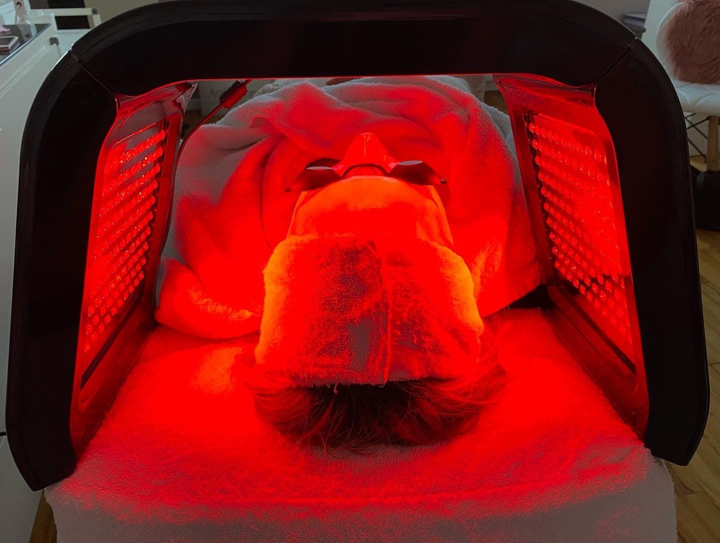 LED-Lichttherapie in Rot über einer zugedeckten Kundin auf der Behandlungsliege, Augen und Gesicht sind geschützt abgedeckt.